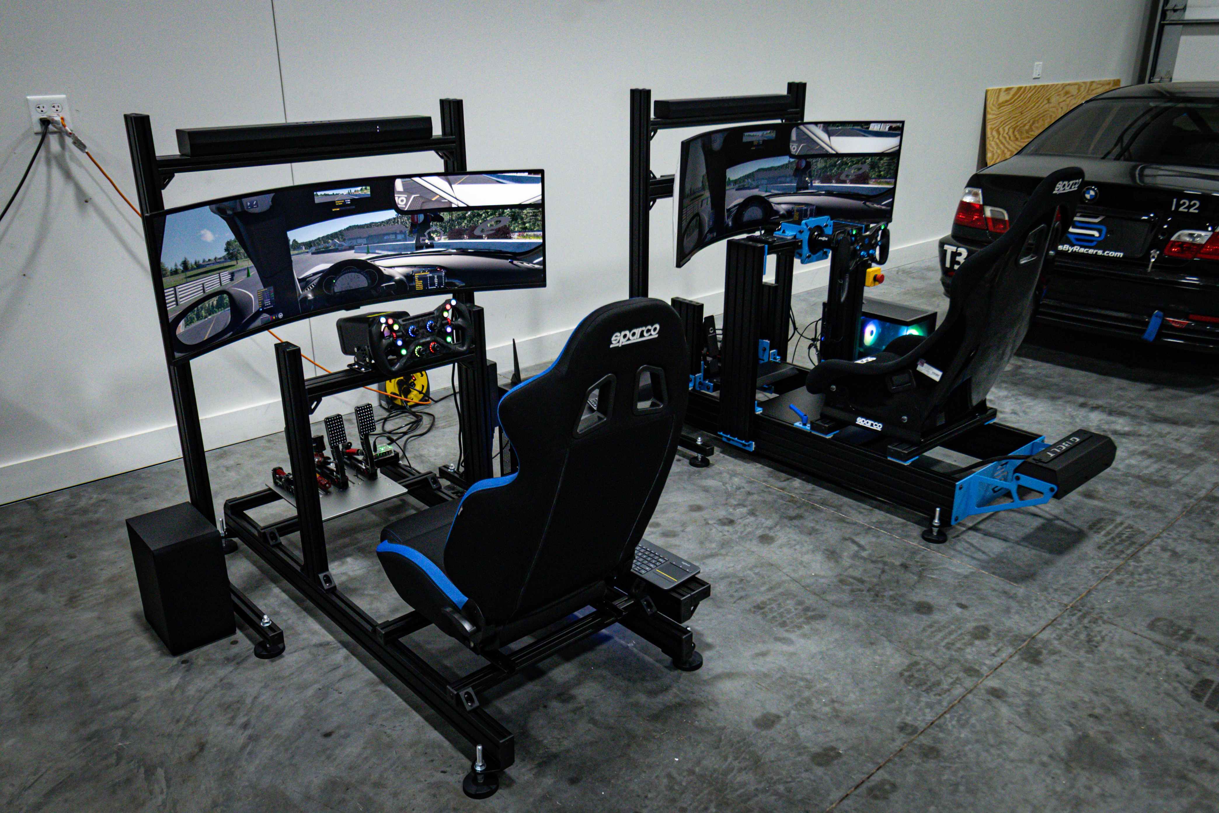 Two Sims By Racers turn-key rigs in the garage beside a BMW race car